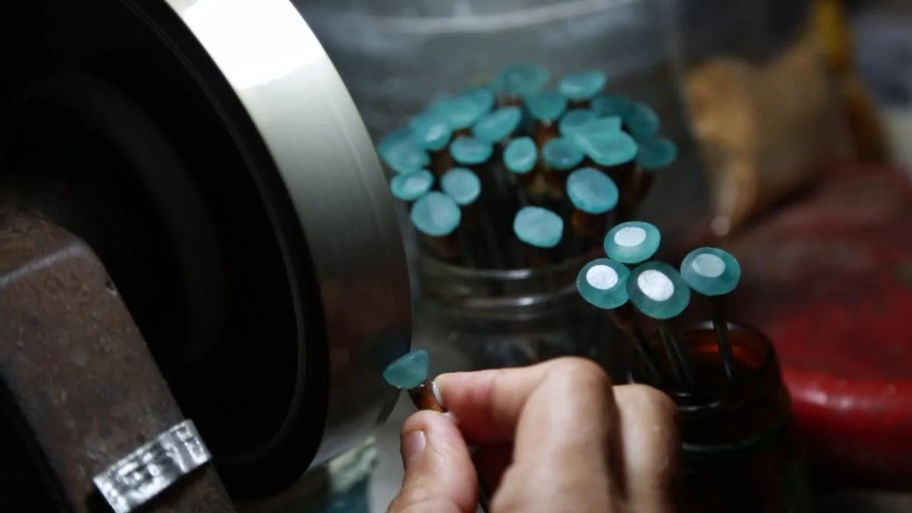 A person crafts a necklace using blue beads, showcasing the art of gem polishing in the process.
