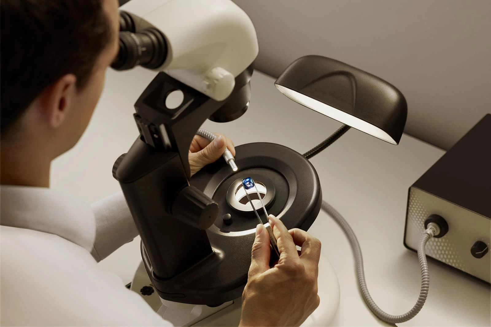 A man examines a small heated gem under a microscope, focusing on its intricate details and characteristics.